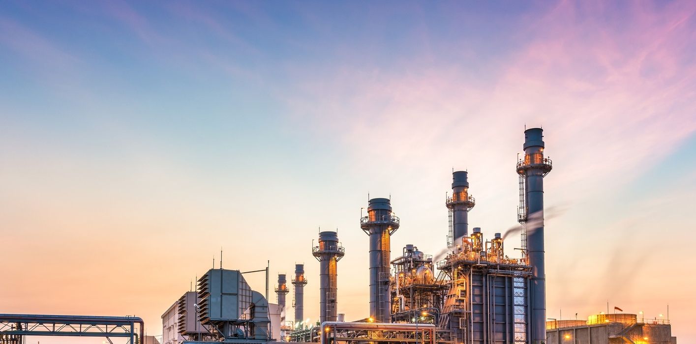 Industrielle Anlage mit mehreren hohen Schornsteinen vor einem pastellfarbenen Himmel